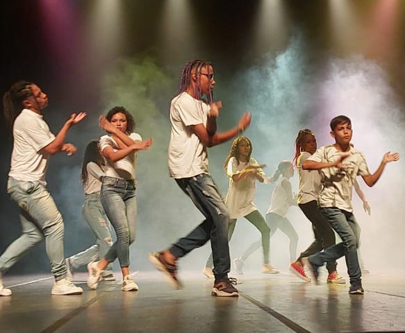 Jovens dançando em palco iluminado em apresentação da OIAEU
